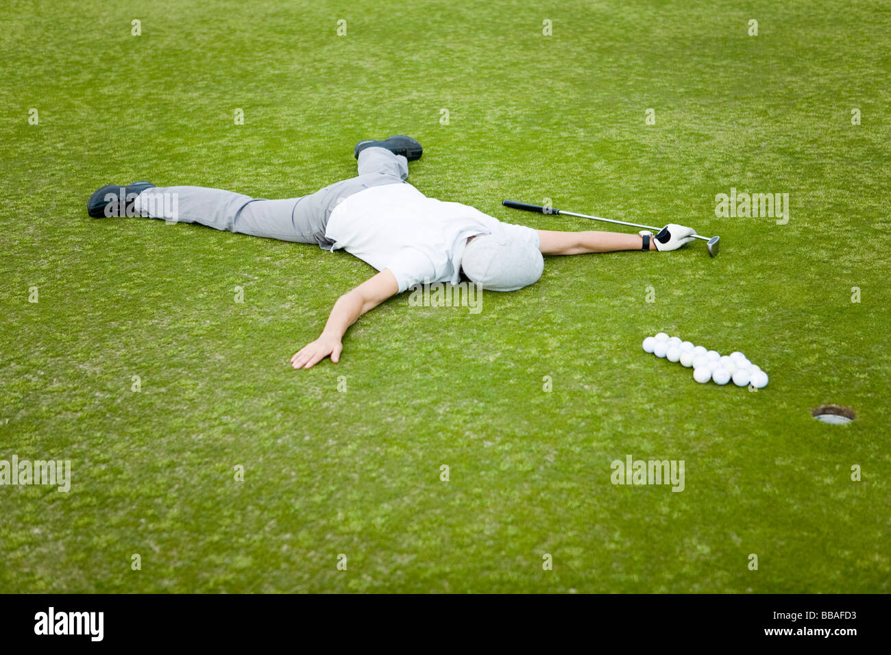 A golfer lying on a putting green behind an arrow of golf balls Stock
