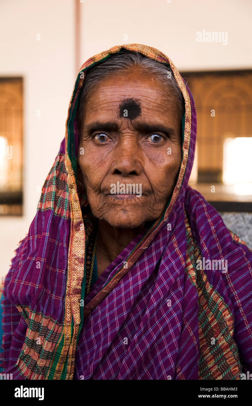 An aged woman with cataracts sits and waits for her train on the platform of Badami railway station in India. Stock Photo