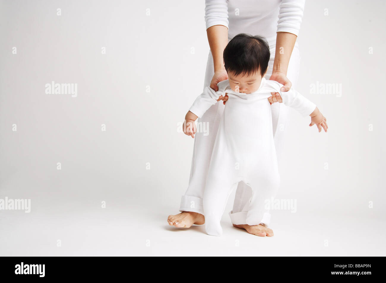 Baby boy standing, being supported by mother from behind Stock Photo Alamy