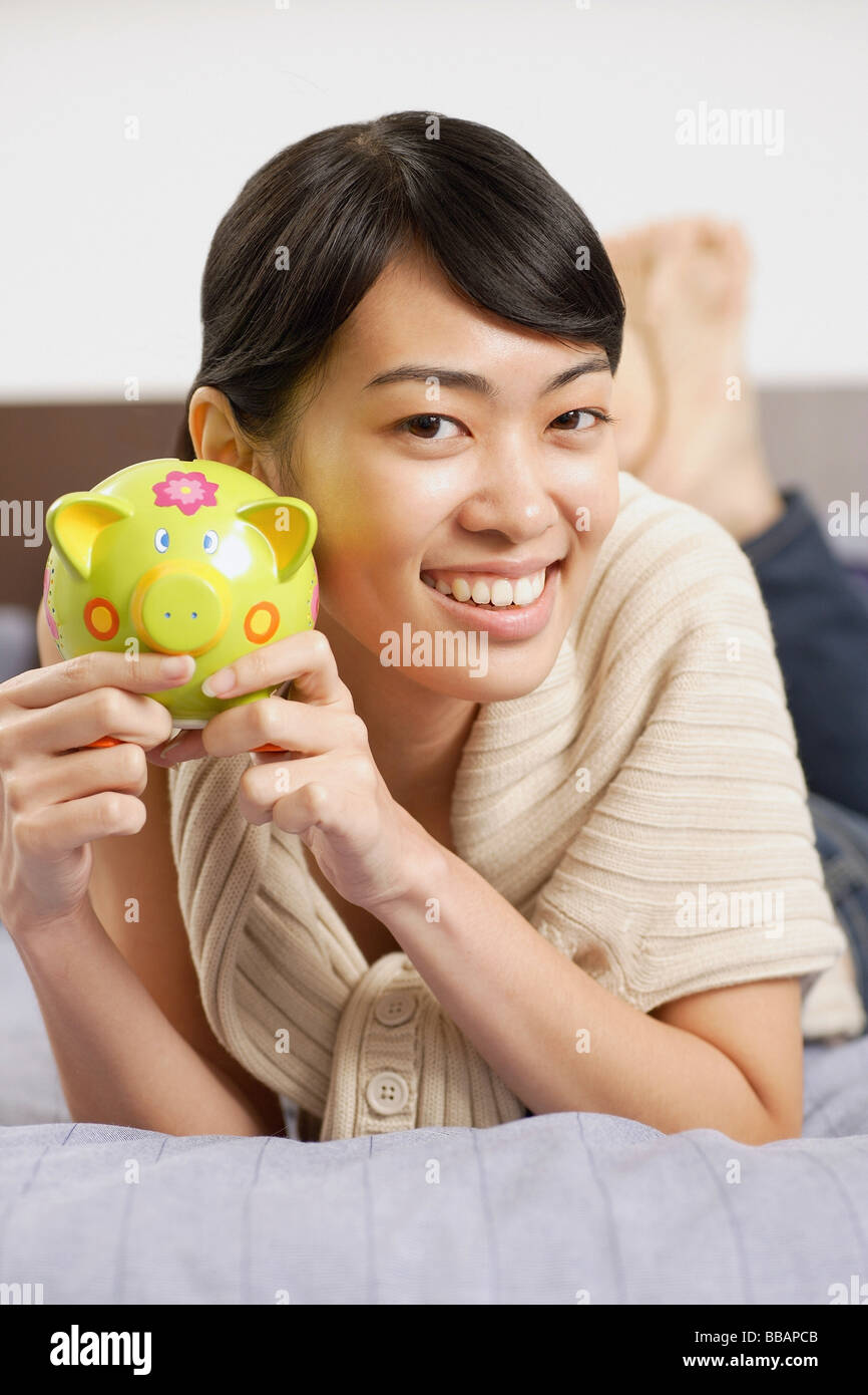 Woman holding piggy bank, lying on bed, smiling at camera Stock Photo ...