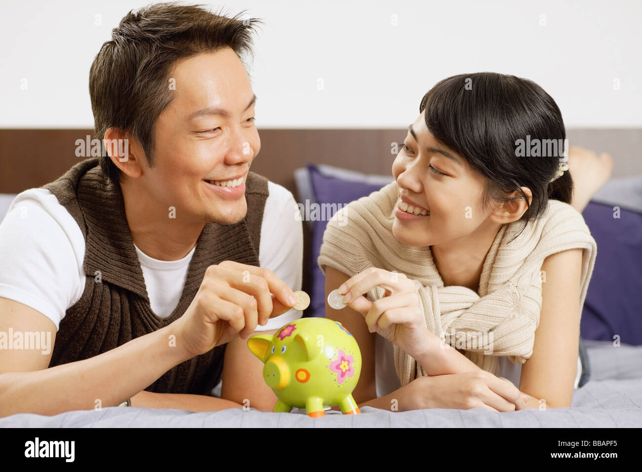 Couple lying on bed, putting coins in piggy bank Stock Photo - Alamy