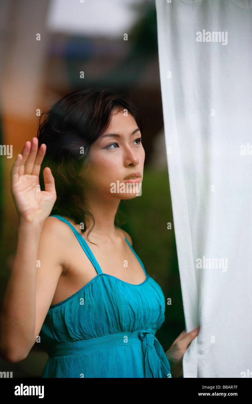 Woman looking through window, holding curtain Stock Photo