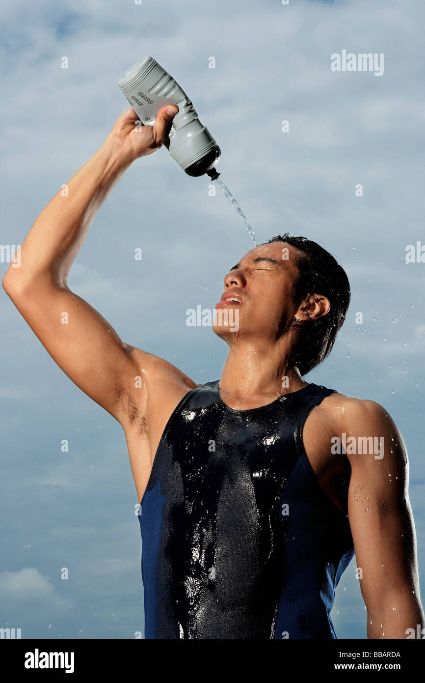 Man squeezing water bottle over face, cooling off after workout Stock