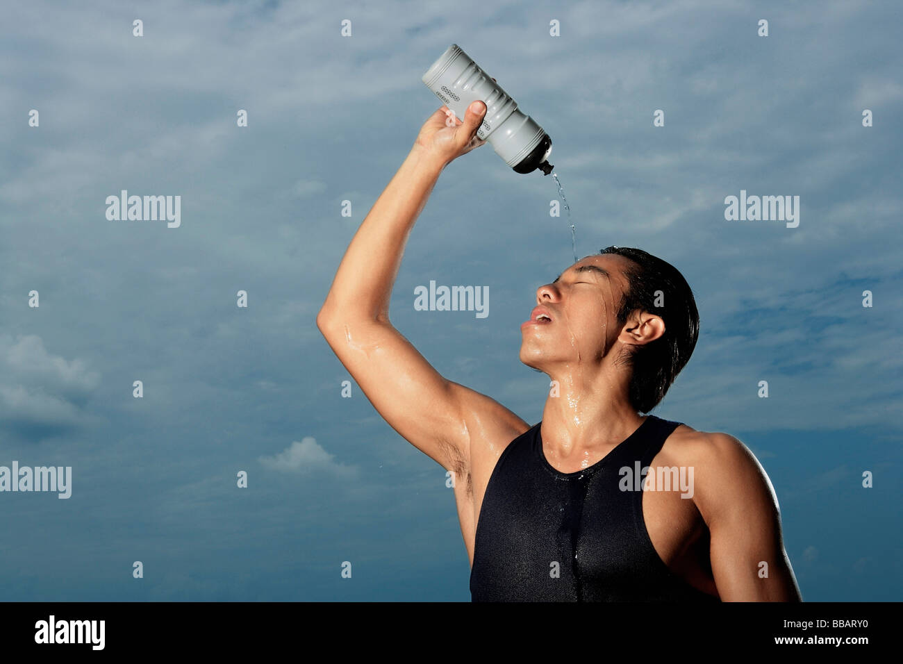 Man squeezing water bottle over face, cooling off after workout, hot