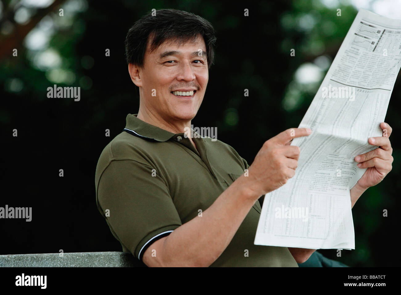 Man sitting on bench in park reading newspaper, smiling at camera Stock ...