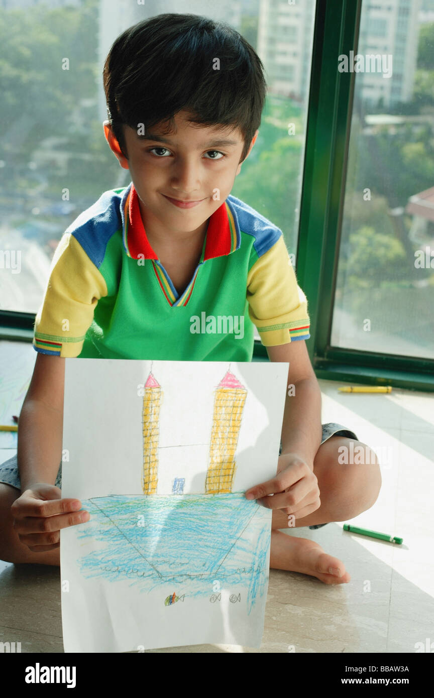 Boy sitting on floor, holding a drawing towards camera Stock Photo