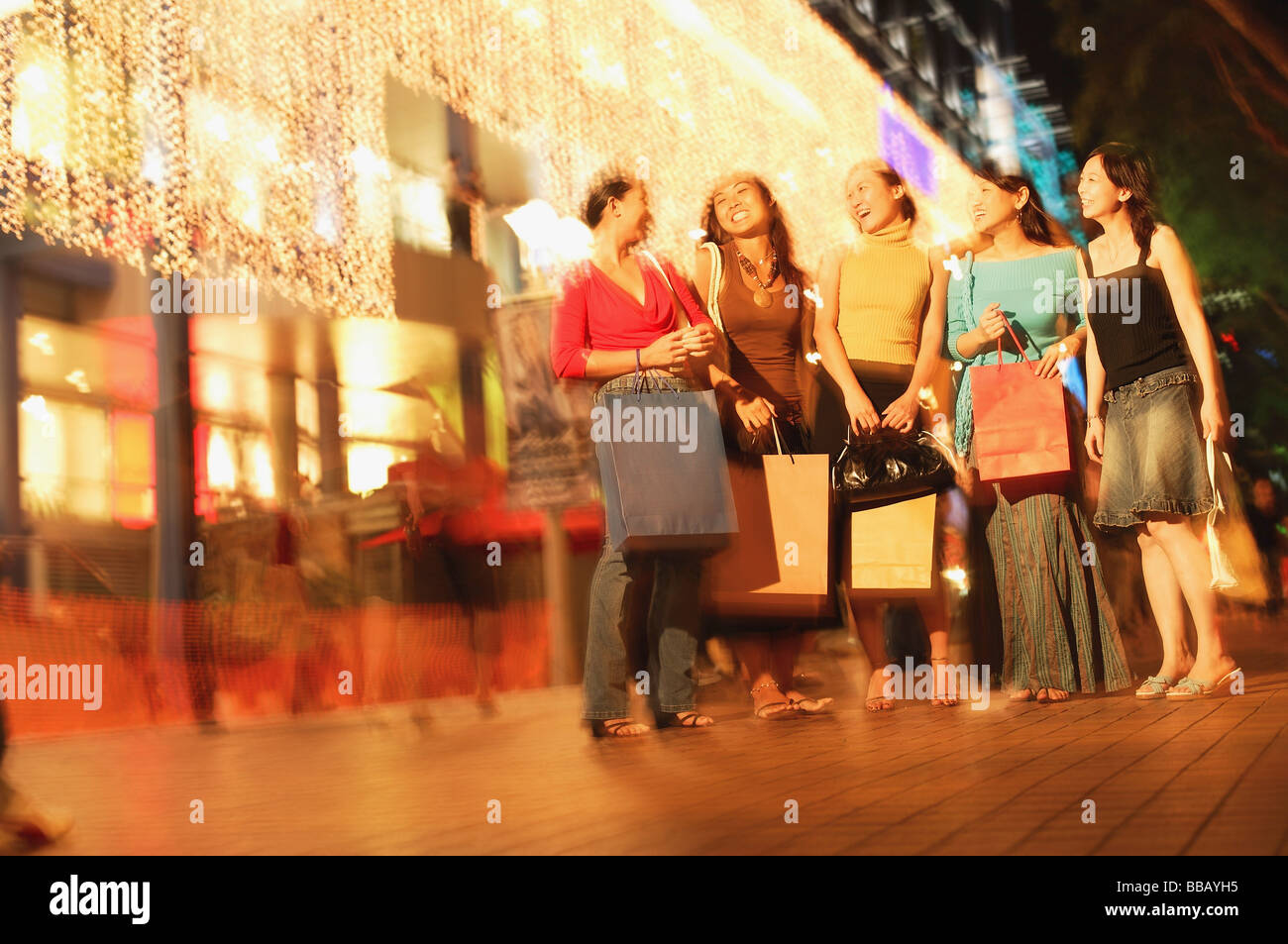 Young women standing side by side, in a row, carrying shopping bags ...