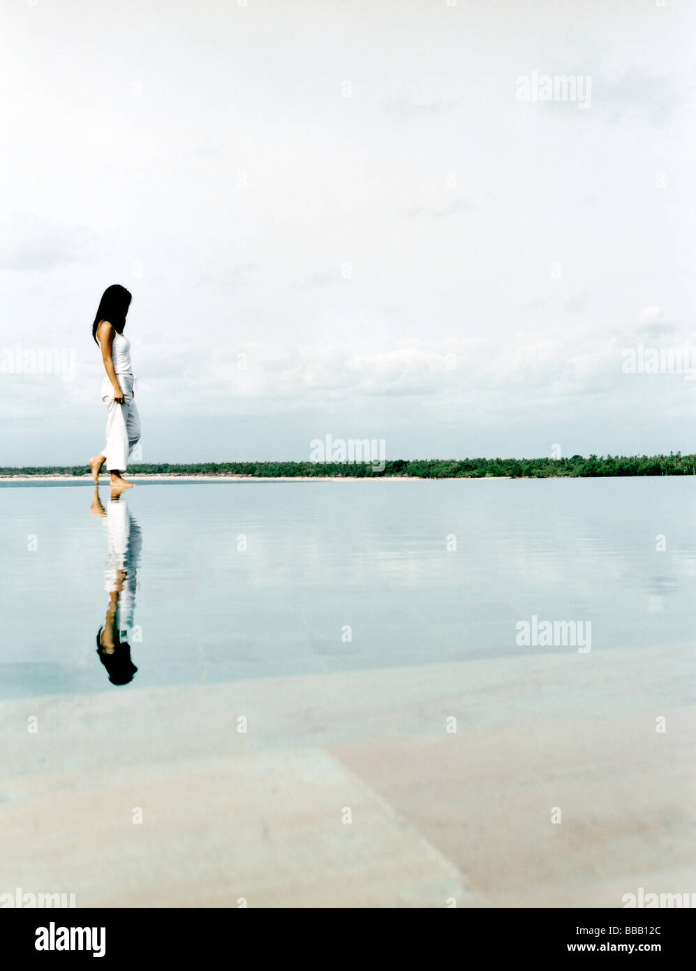 Woman walking on water's edge with reflection Stock Photo - Alamy