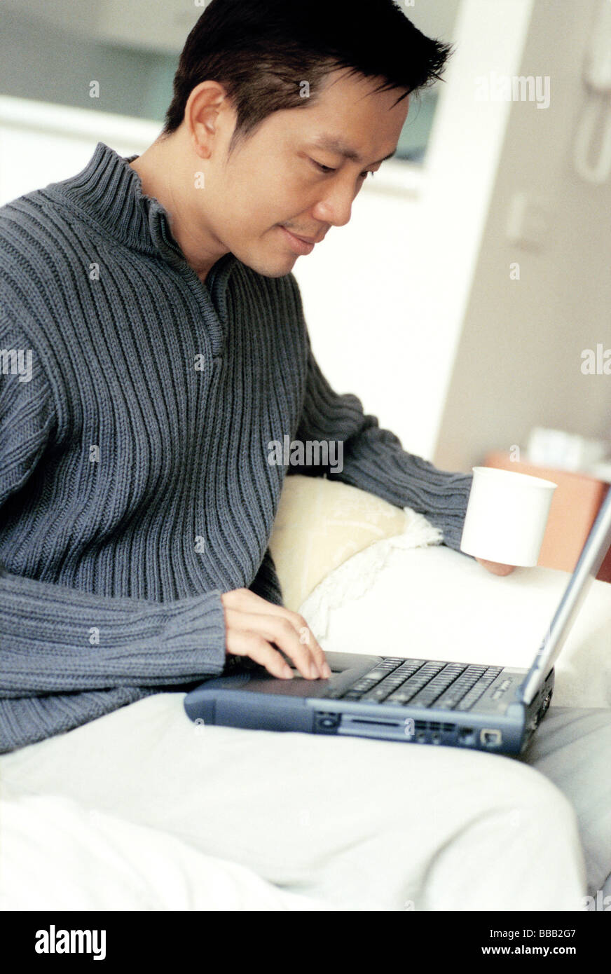 Man sitting cross-legged using laptop holding cup Stock Photo