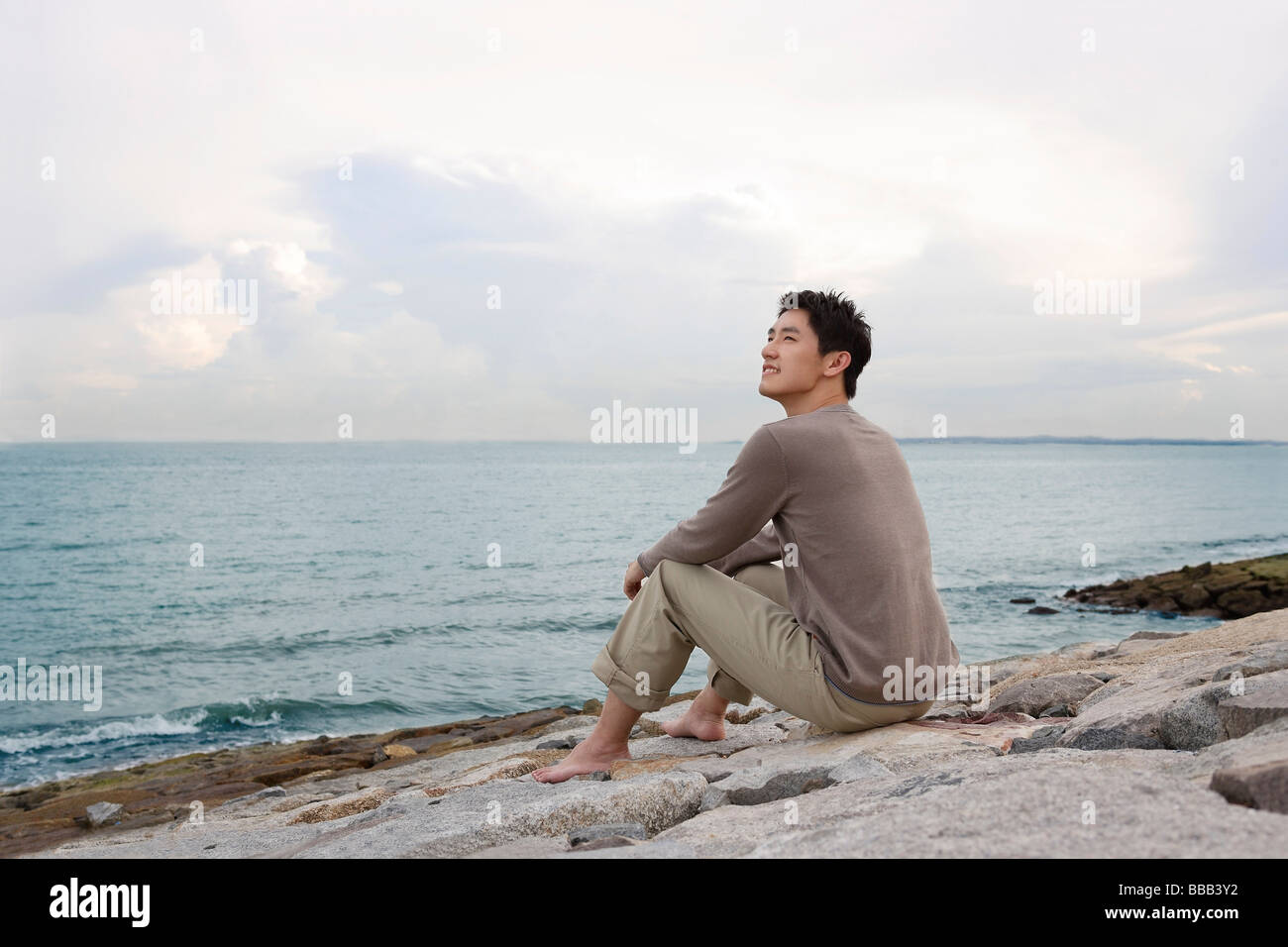 Man sitting by shore looking out to sea Stock Photo - Alamy