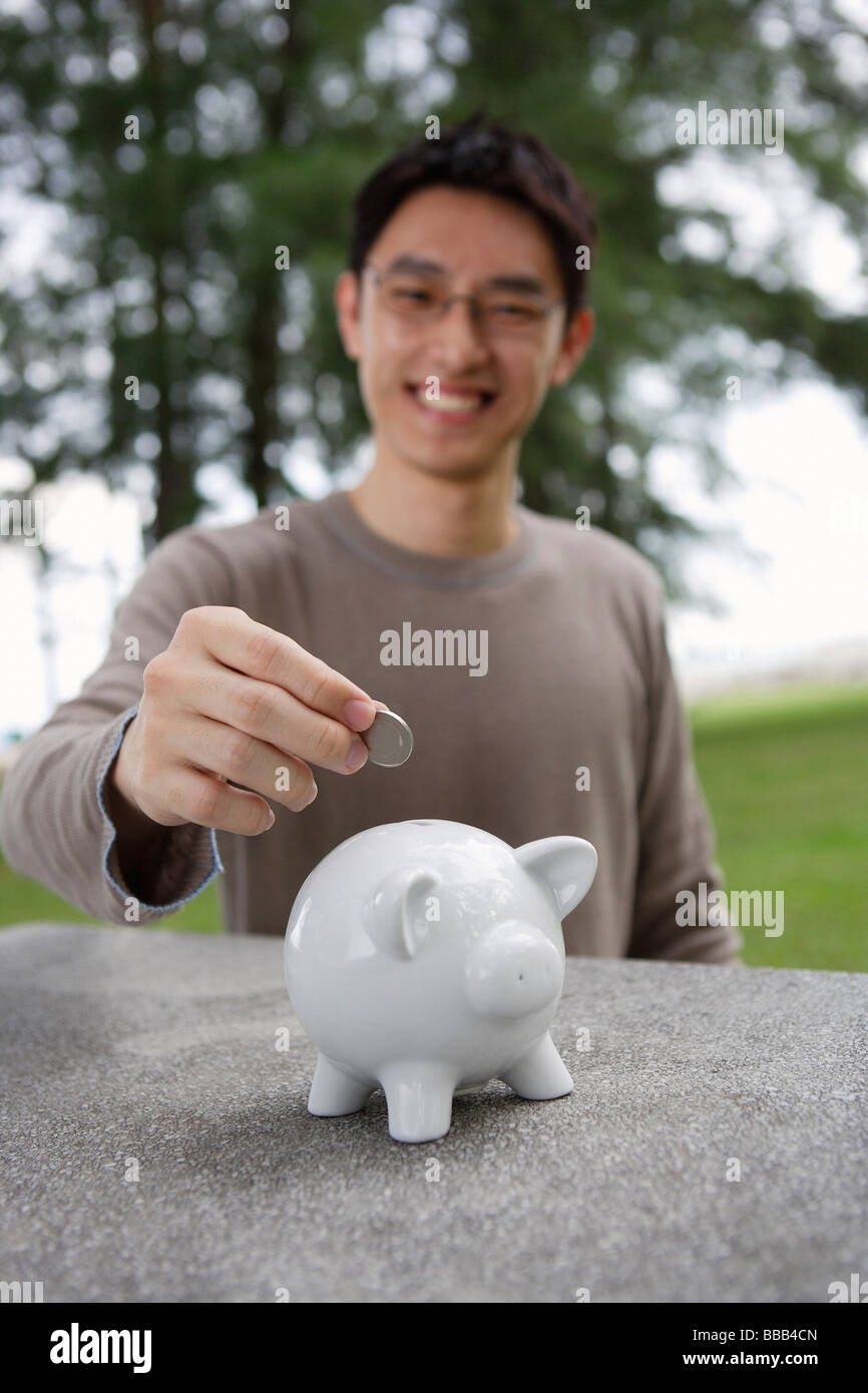 Man putting coin into piggy bank Stock Photo - Alamy