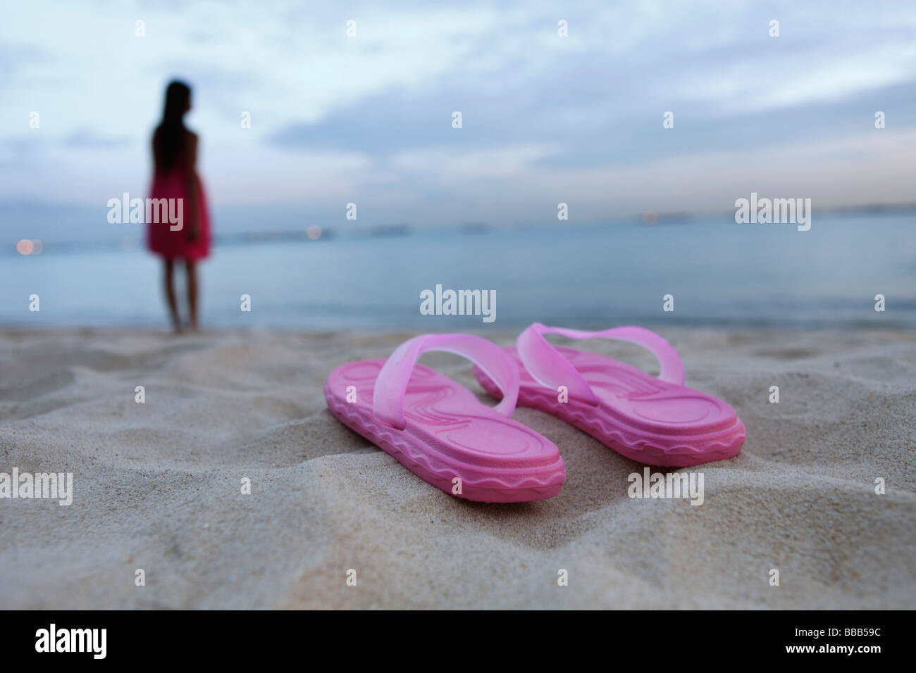 Sandals on sandy beach, woman in background Stock Photo