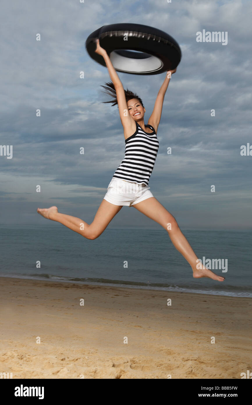 Young woman jumping on beach, holding up inner tube Stock Photo Alamy