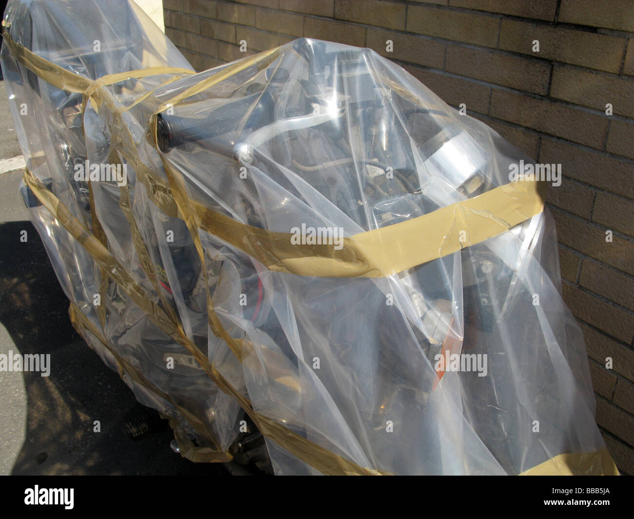 one old motorbike covered with polythene plastic sheet in street road ...