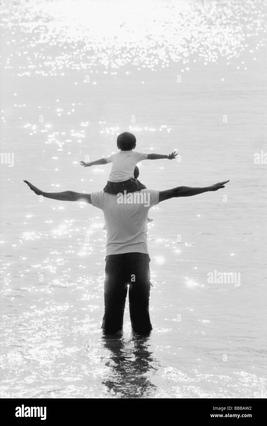 Father and son wading in water, son on father's shoulders, arms