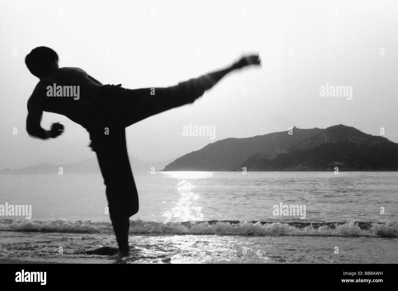 Man kicking in Kung Fu (Wu Shu) pose on beach, silhouette Stock Photo