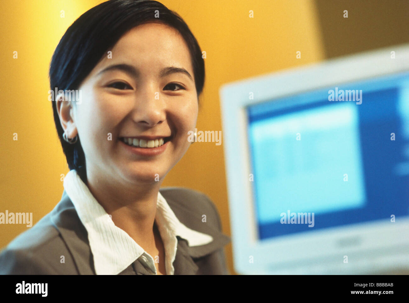 Female executive smiling with computer monitor in background Stock