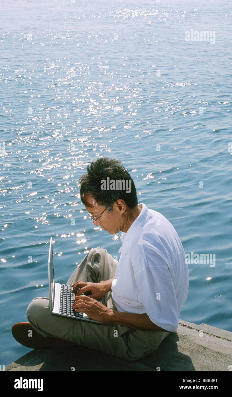 Man using laptop, sea in background Stock Photo - Alamy