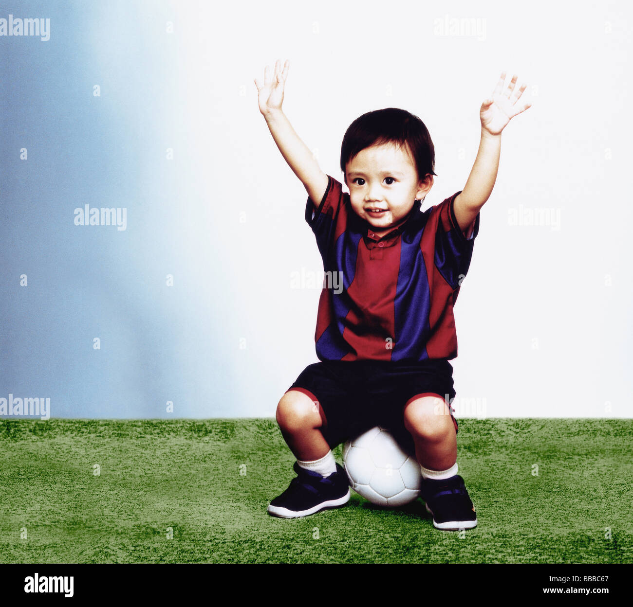 Young boy sitting on soccer ball with arms in the air Stock Photo