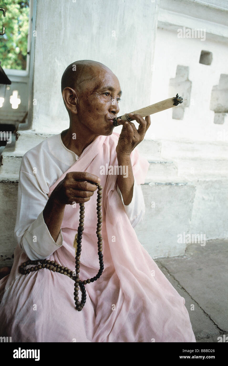 Myanmar, Mandalay area, Nun smoking cigar while holding prayer beads Stock Photo