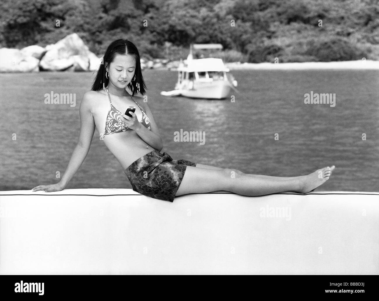 Teenage girl in bikini using cellular phone, boat in background Stock Photo