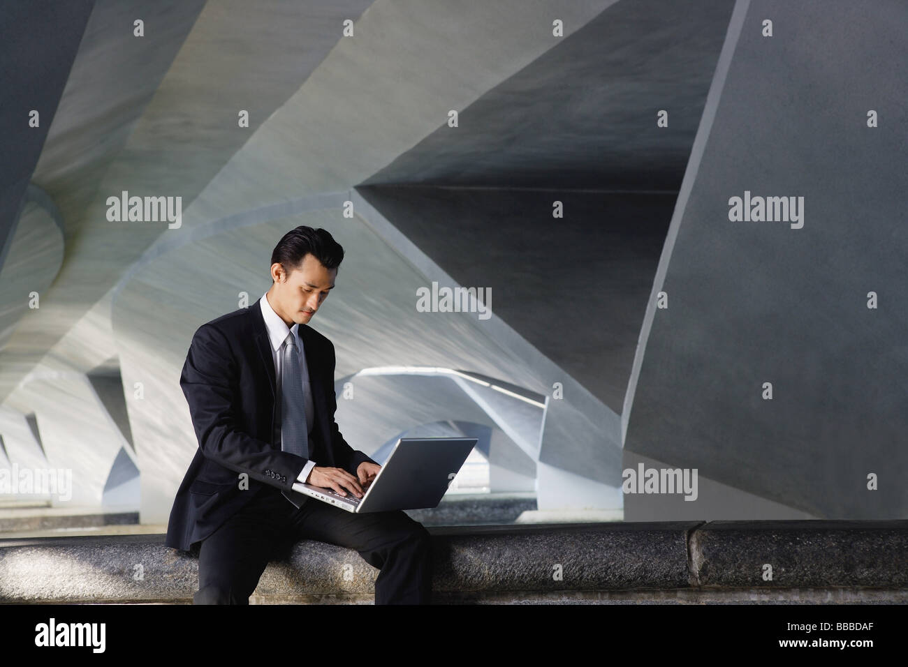 Businessman sitting on ledge, using laptop Stock Photo - Alamy