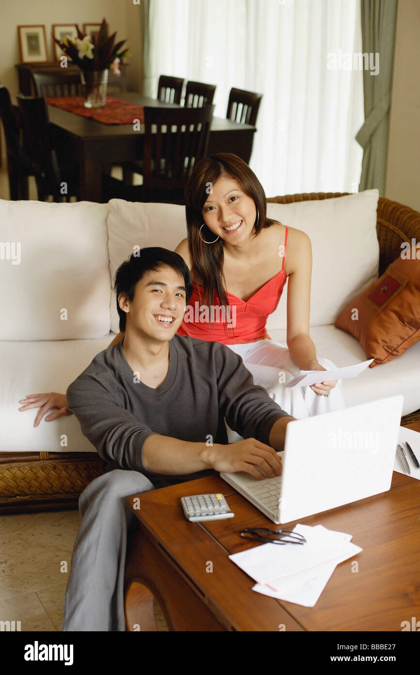 Couple in living room, using laptop, looking at camera Stock Photo - Alamy