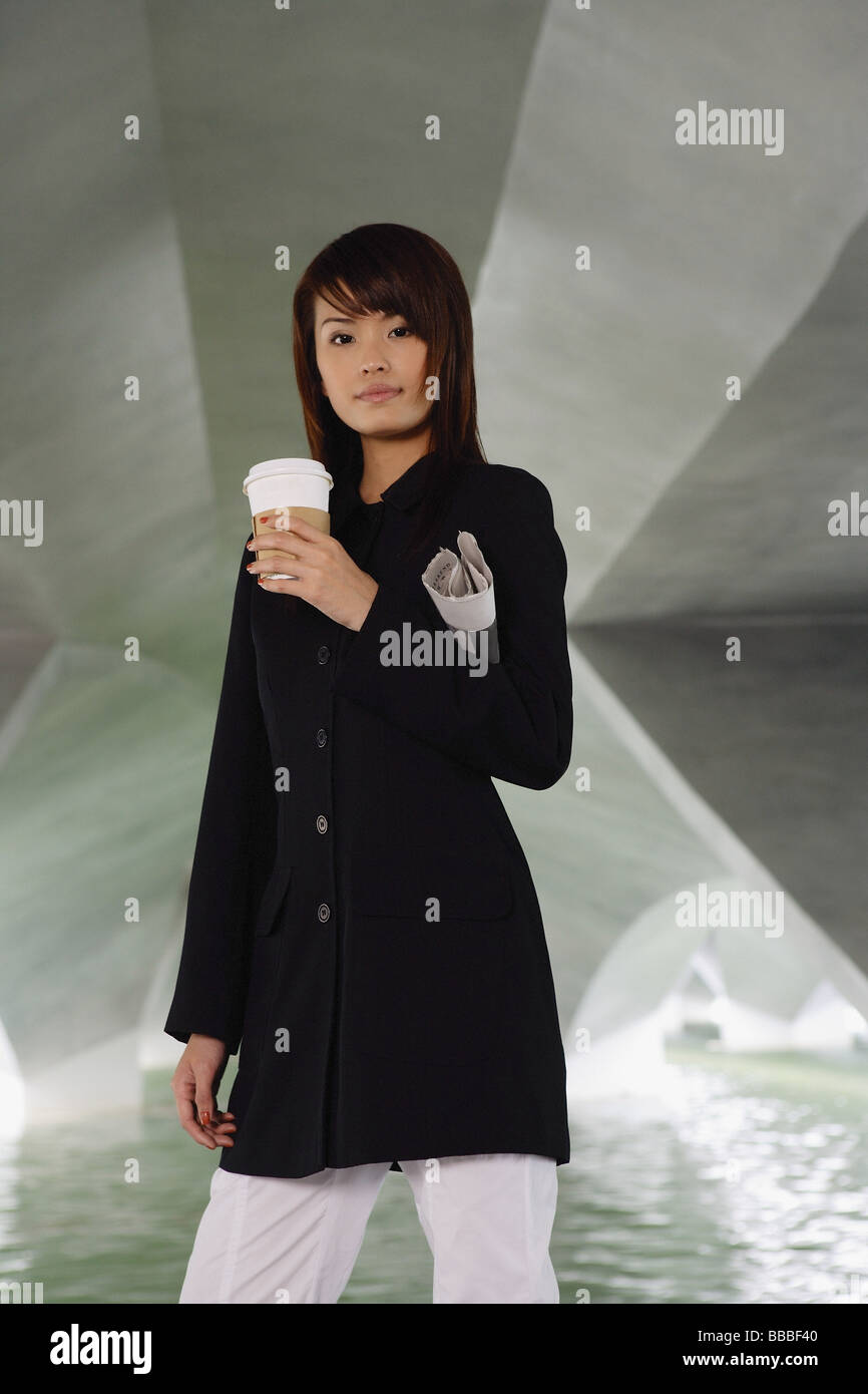 Woman in black jacket, holding disposable coffee cup and newspaper ...