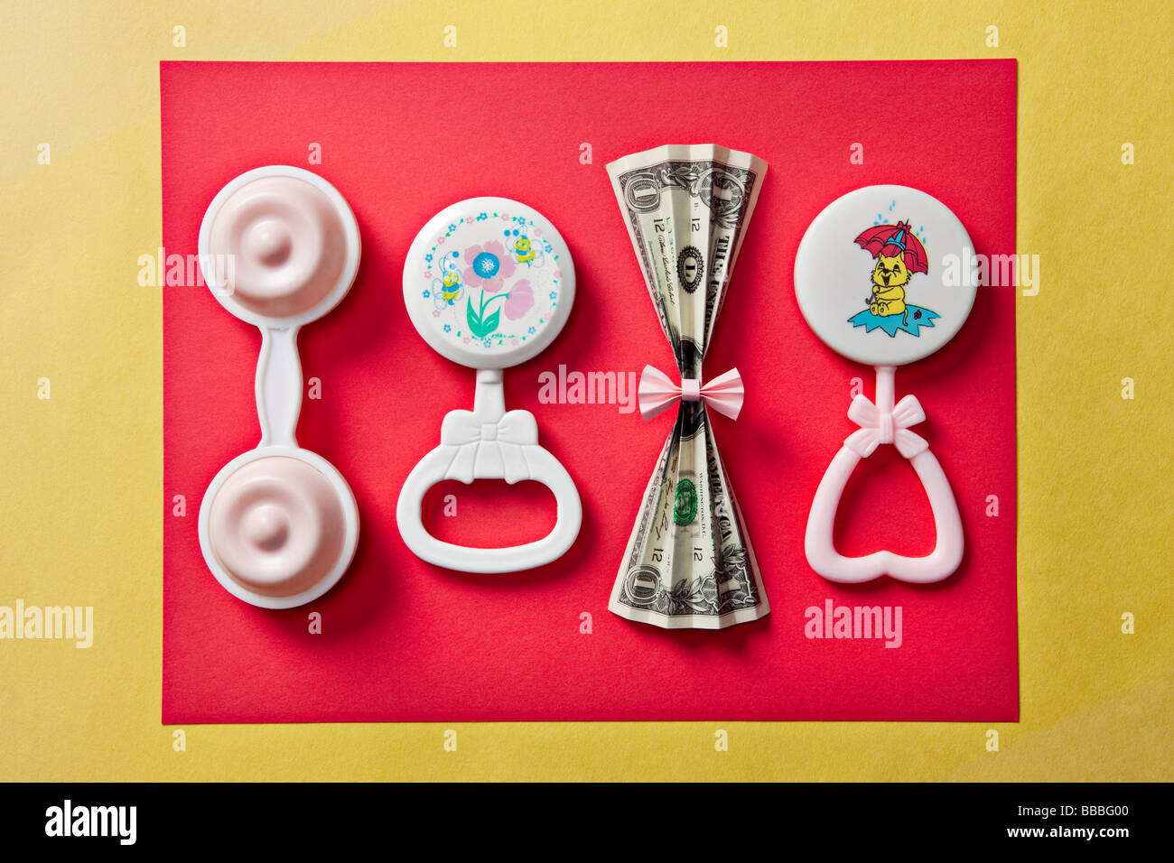 baby rattles and dollar bill on red and yellow background Stock Photo