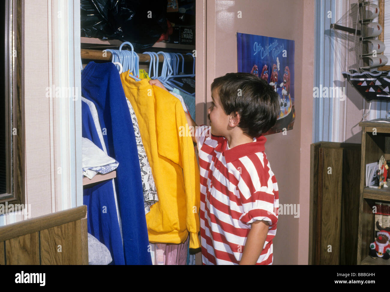 Boy choose select decide shirt clothes wear closet hang neat clean chore Stock Photo