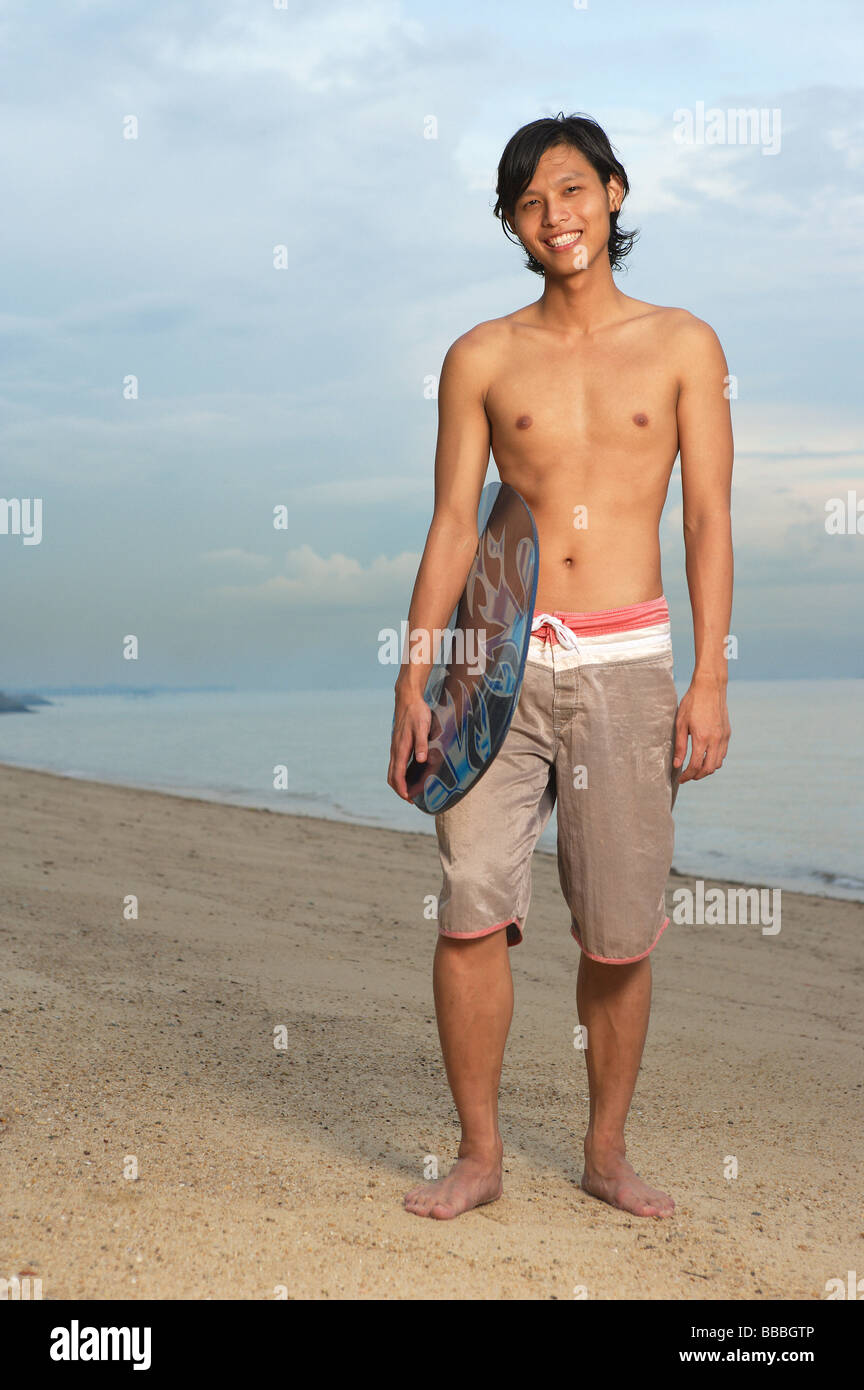 Young man holding skimboard, standing on beach Stock Photo