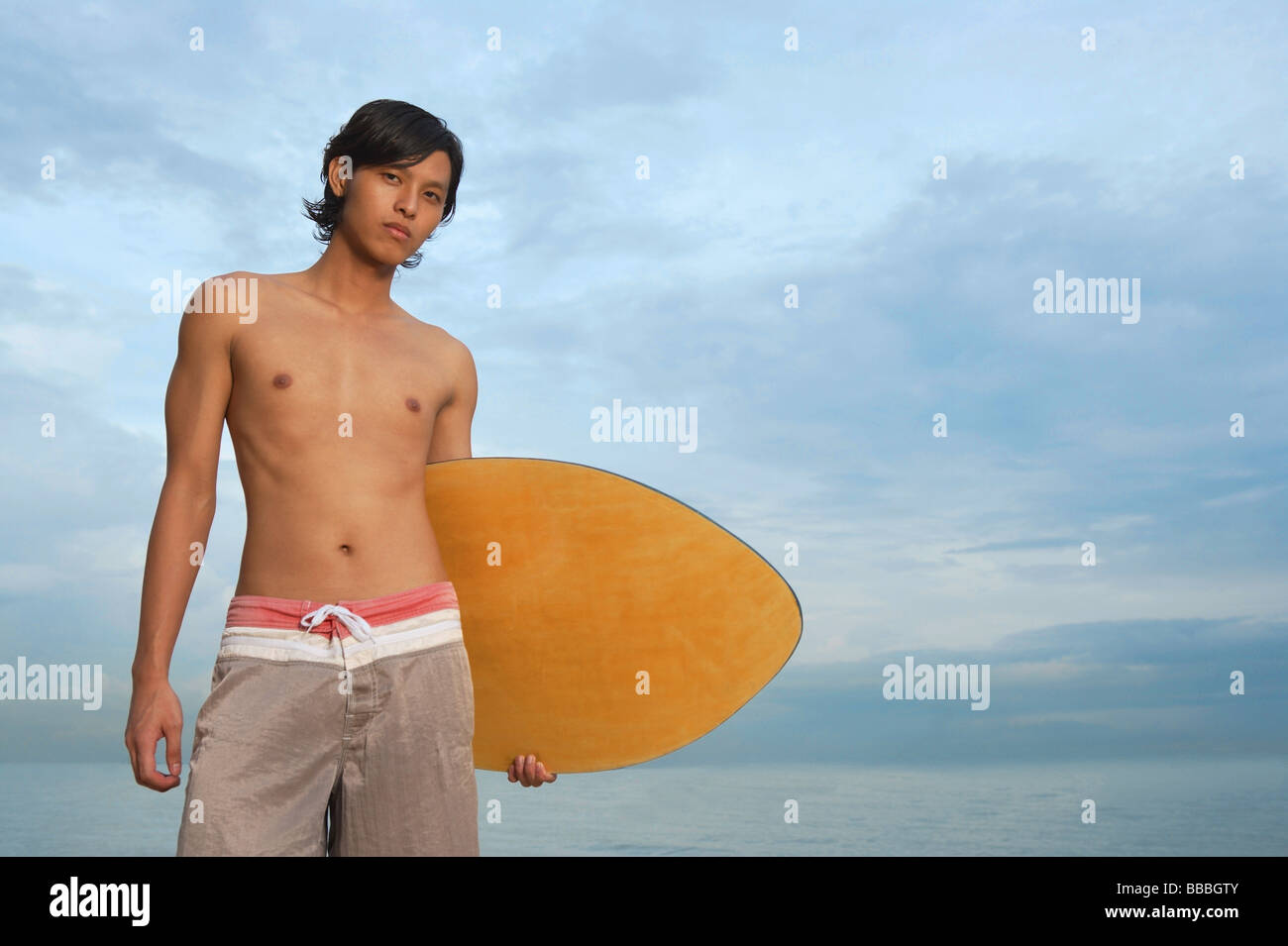 Young man with skimboard, looking at camera Stock Photo