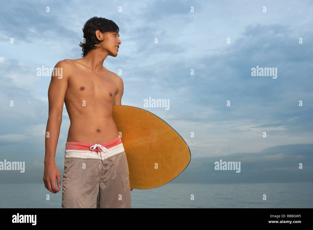 Young man with skimboard, looking away Stock Photo