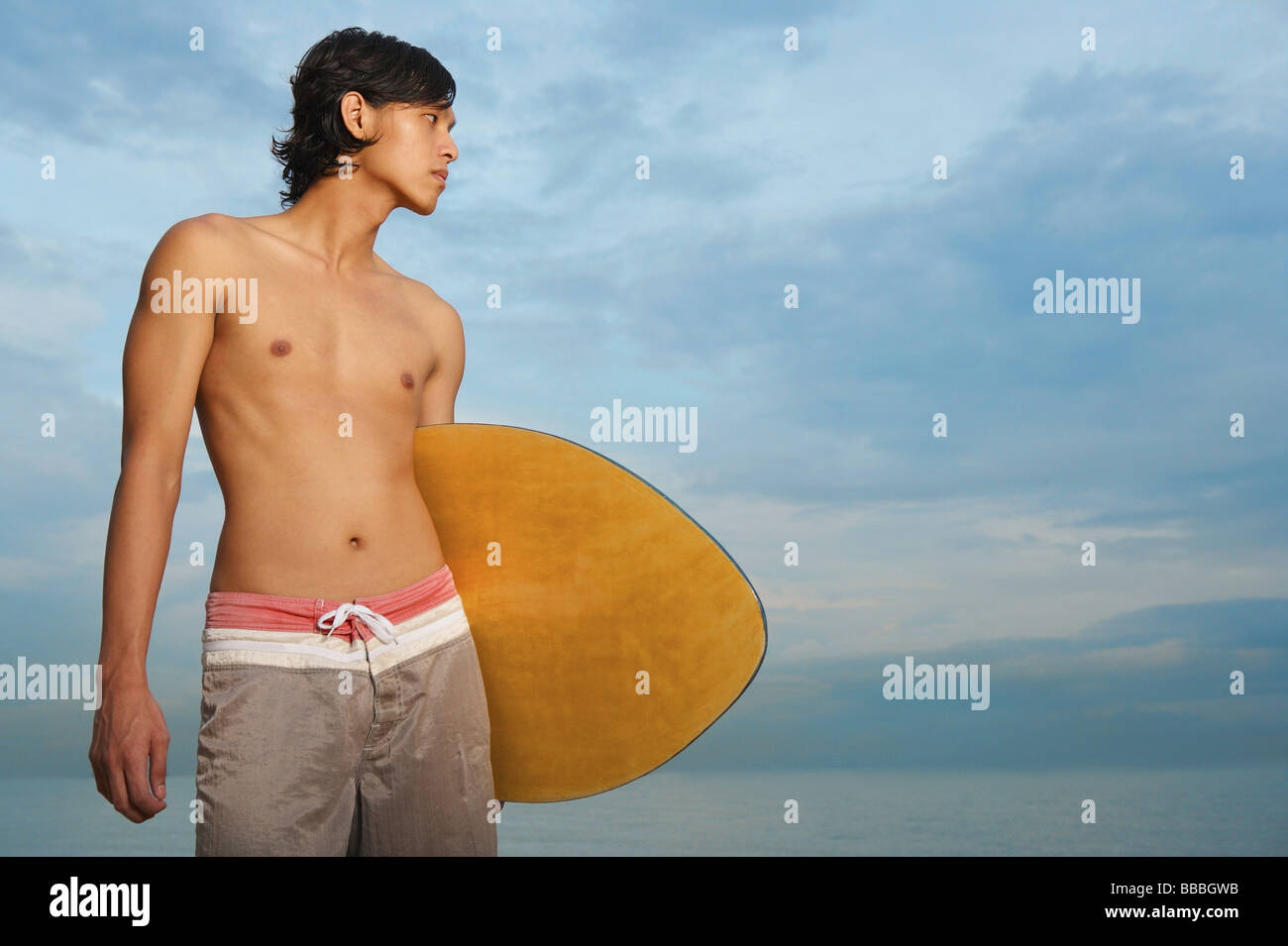 Young man holding skimboard, looking away Stock Photo