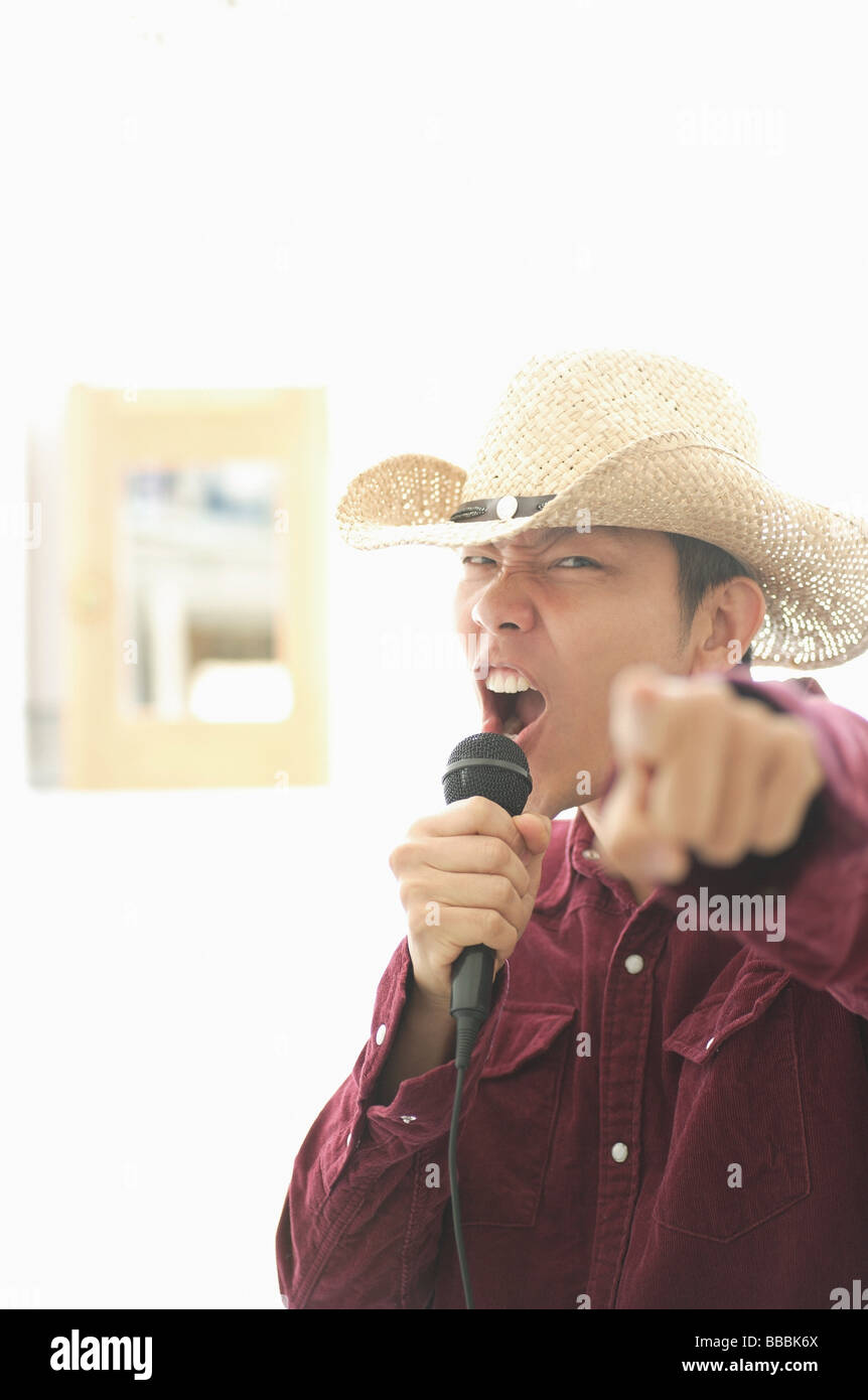 Man wearing hat, holding mike, singing and pointing at camera Stock Photo