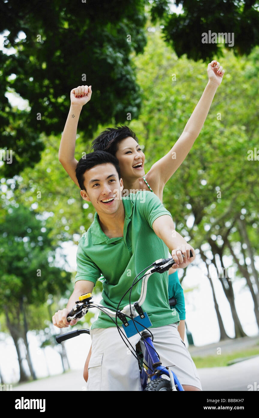 Couple on tandem bicycle, woman raising arms in the air Stock Photo