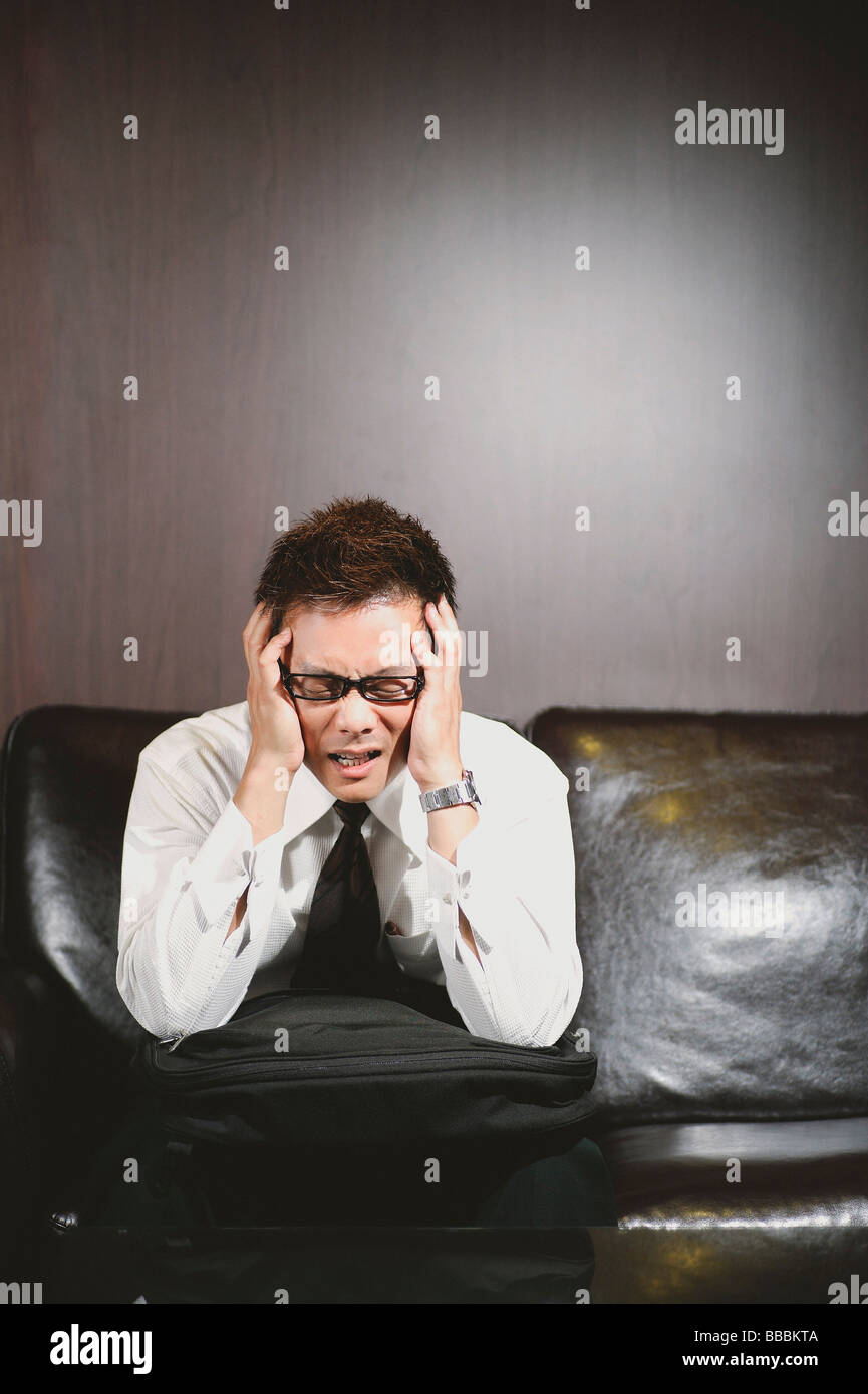 Businessman sitting on sofa, hands on either side of his head, anguished expression Stock Photo