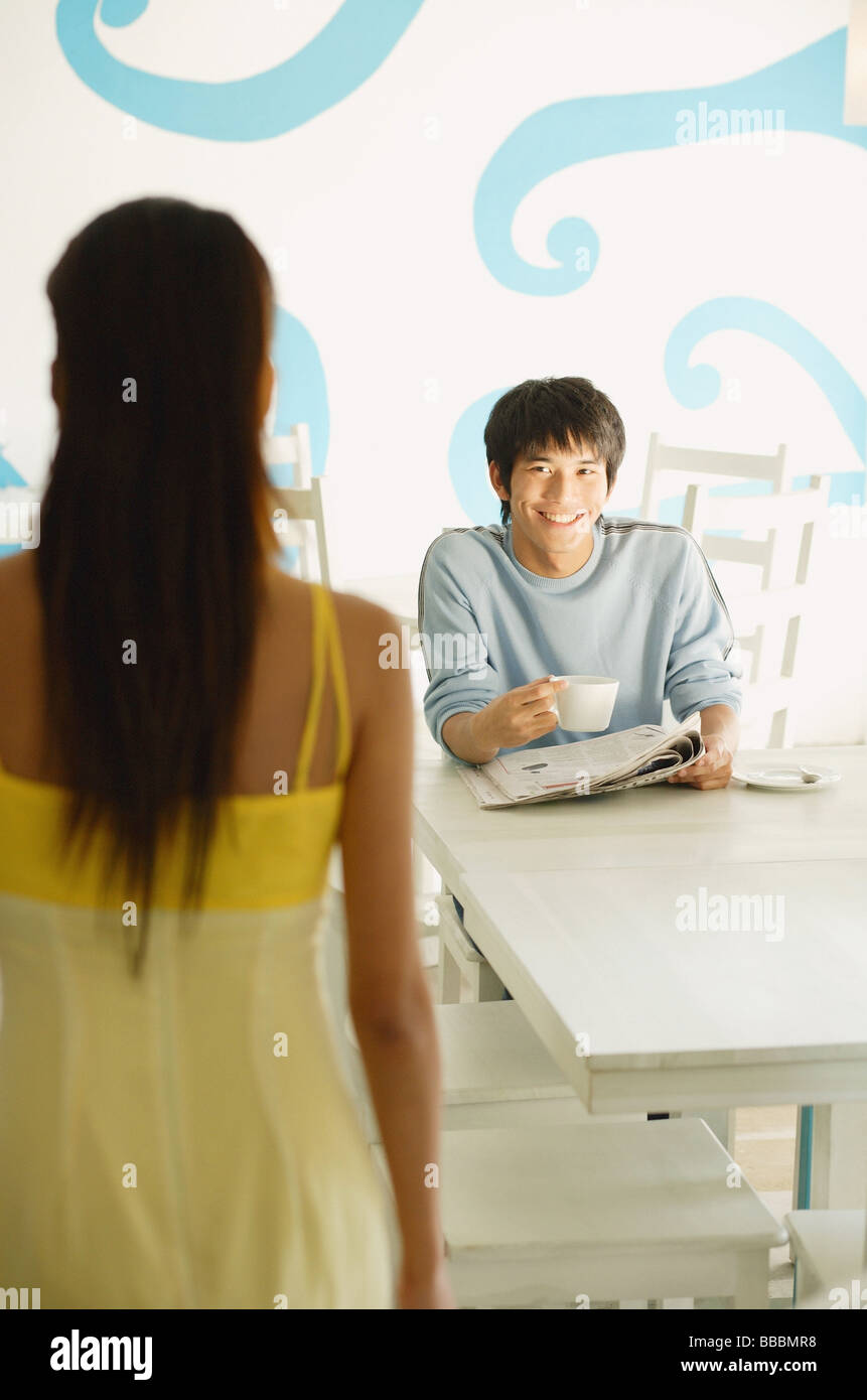 Man sitting at table with newspaper and cup, smiling at woman standing in front of him Stock Photo