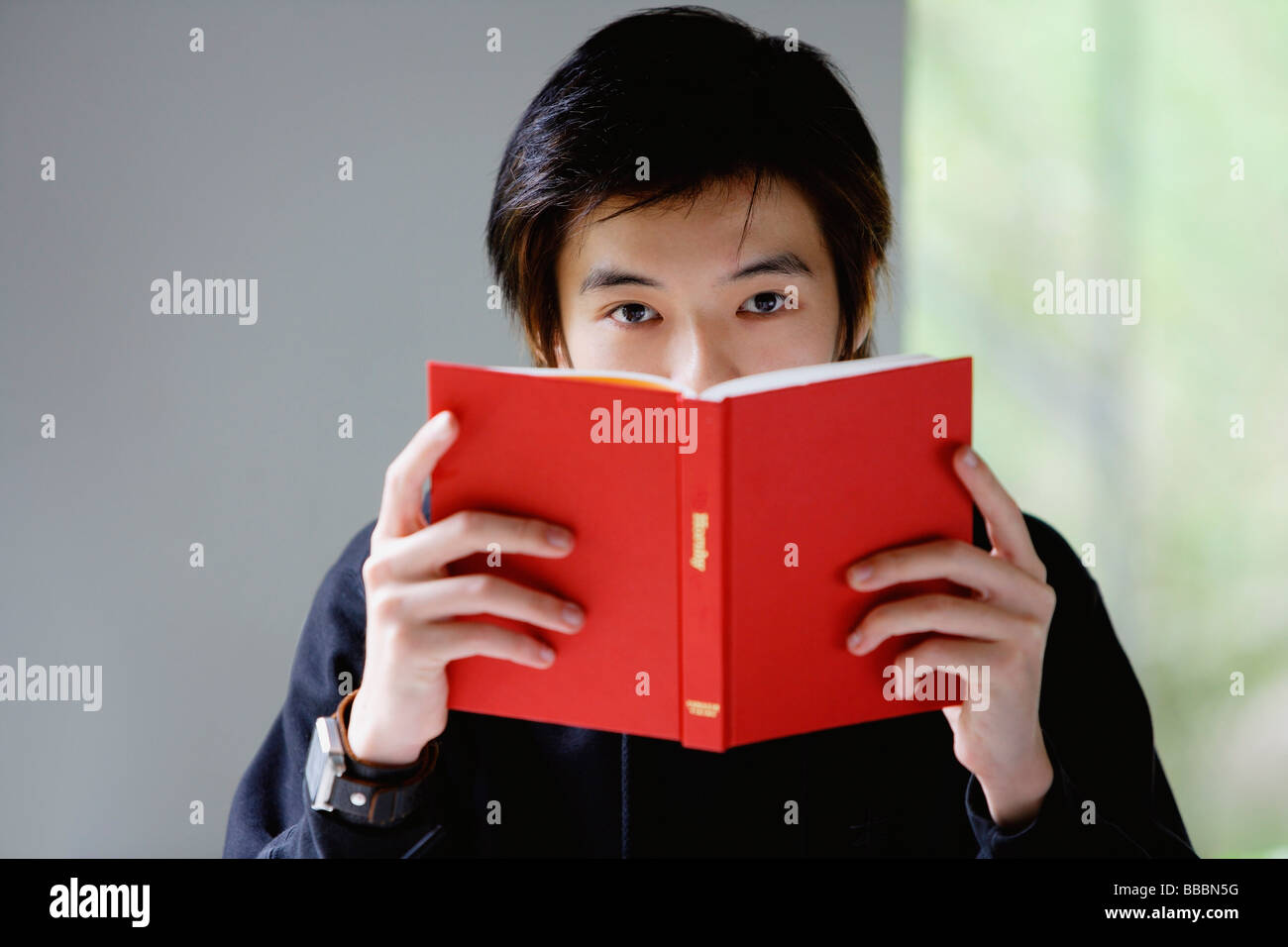 Young man with book covering his face, looking at camera Stock Photo ...