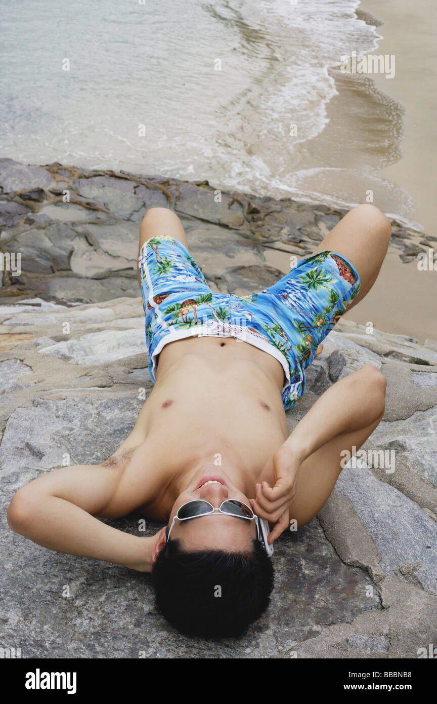 Man lying on rocks at beach, using mobile phone Stock Photo
