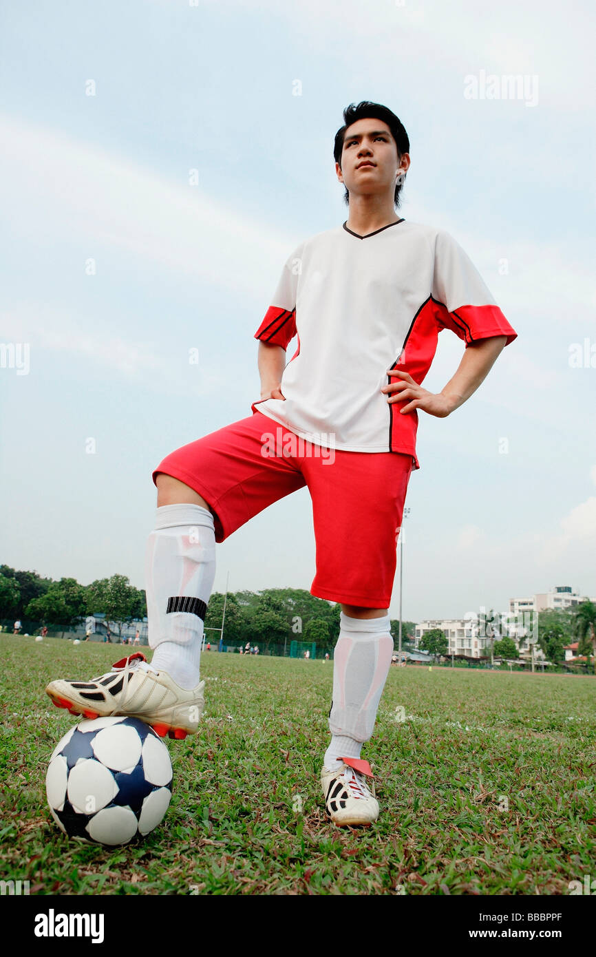 Soccer player standing with one foot on ball and hands on hips Stock
