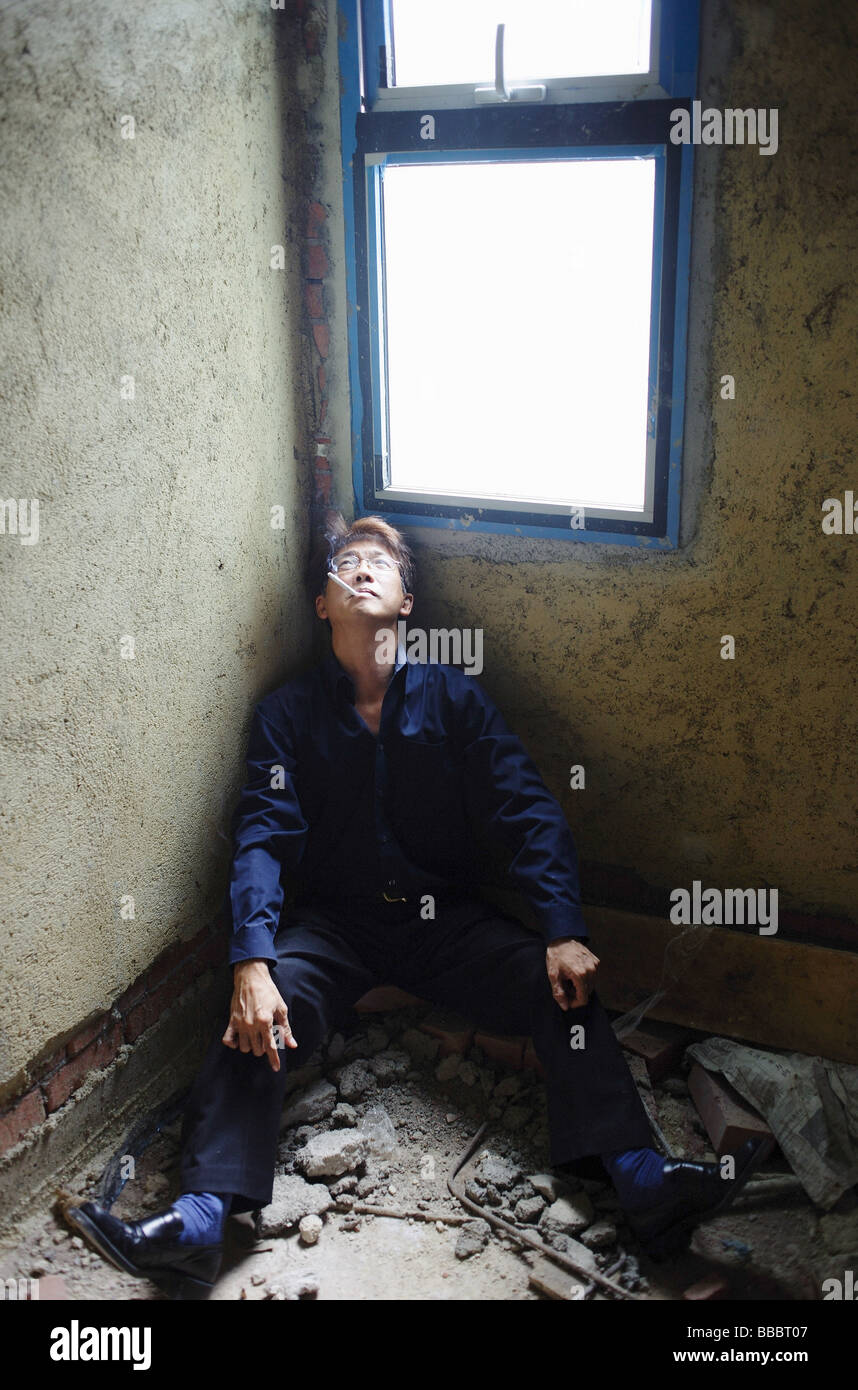 Man sitting in corner of empty room, smoking Stock Photo