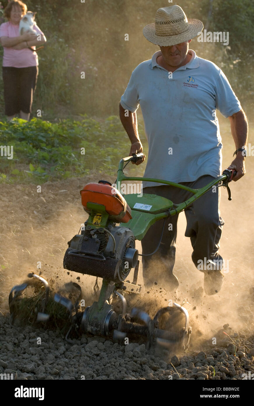 Farmer ploughing up field with cultivator while his wife watches in