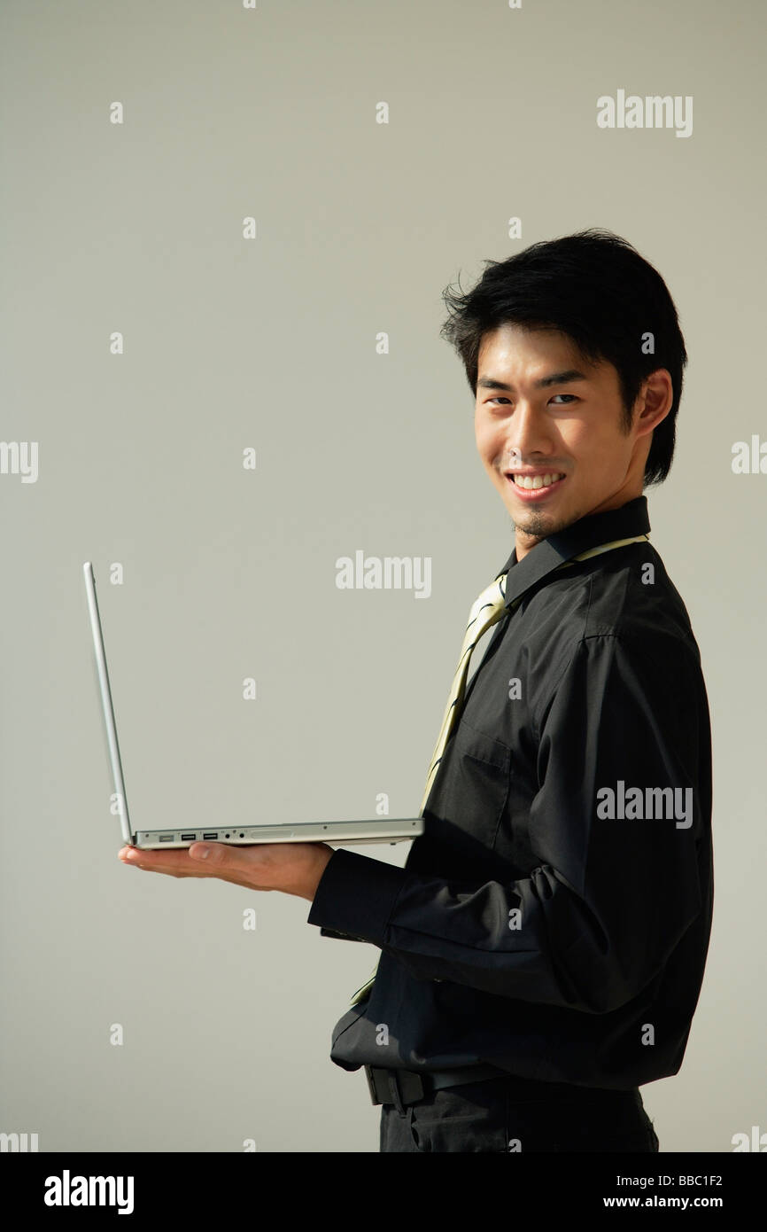 Young man with laptop on one hand smiling at camera Stock Photo - Alamy