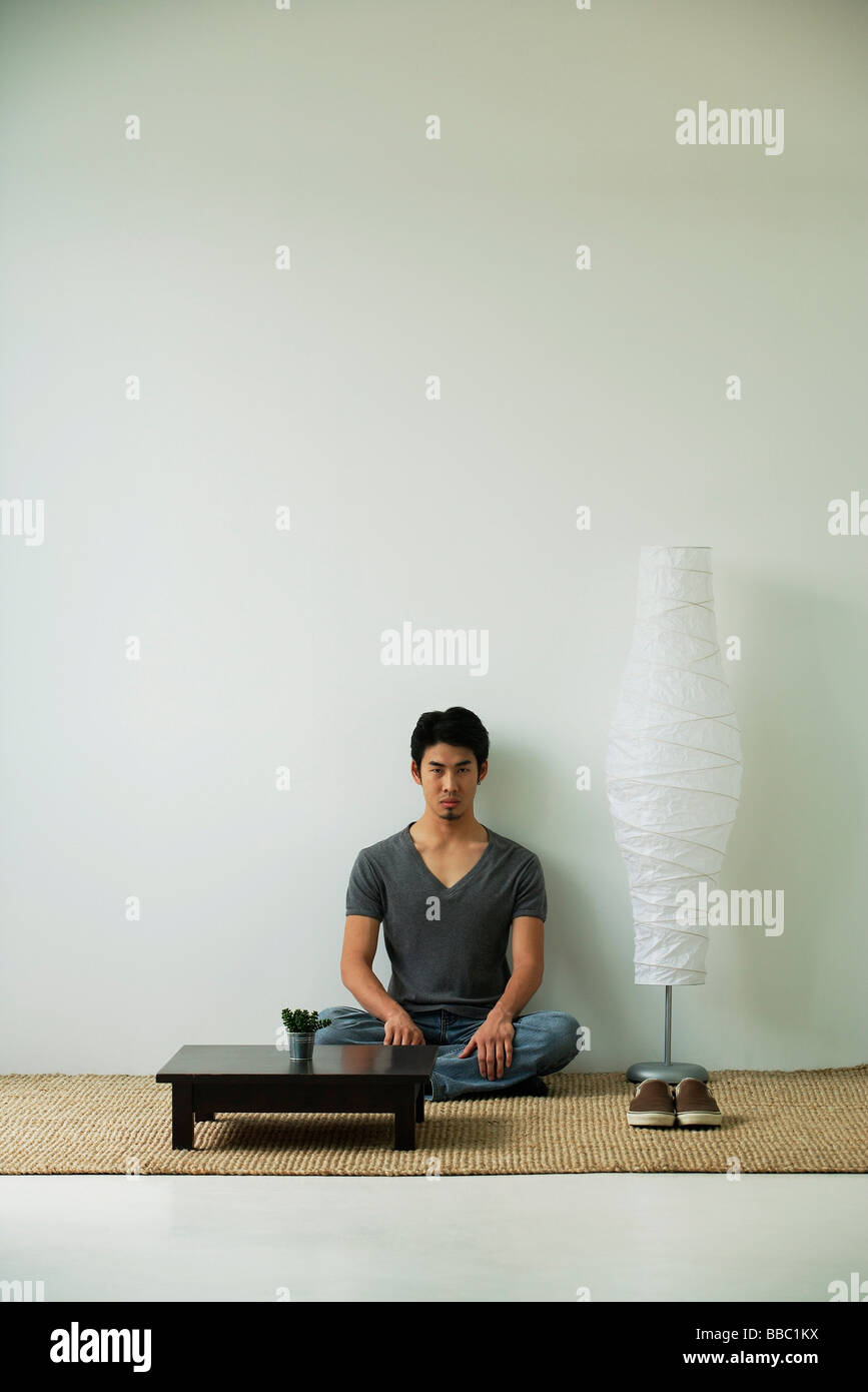 Serious young man sitting on floor, looking at camera Stock Photo - Alamy