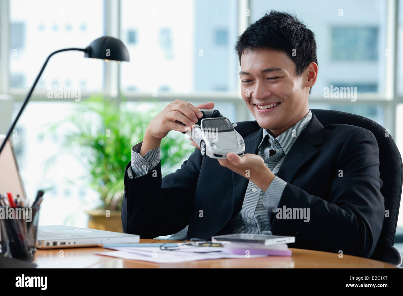 A man plays with a toy car on his desk Stock Photo