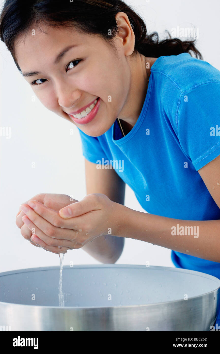 A young woman smiles at the camera as she washes her face Stock Photo