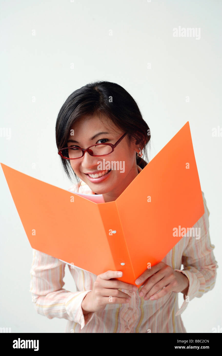 A woman smiles at the camera as she holds an orange folder Stock Photo