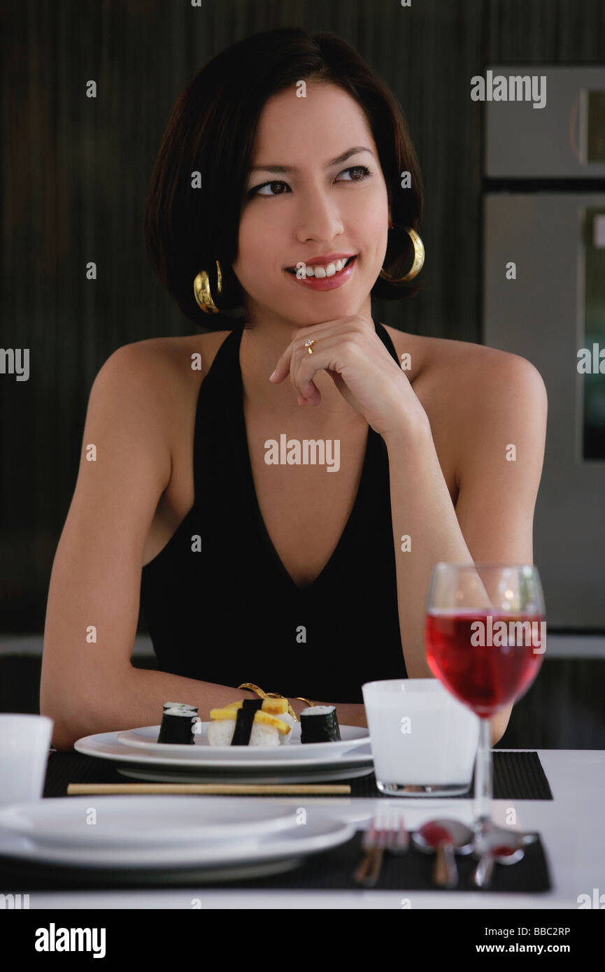 A woman sits at a table with a plate of sushi and a glass of red wine Stock Photo