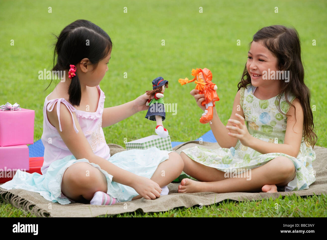 Two girls sitting on picnic blanket, playing with dolls Stock Photo